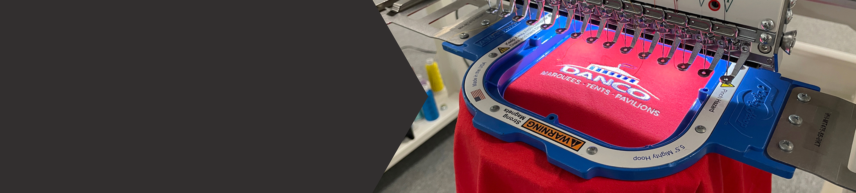 Close up of a Danco logo on a red shirt being embroidered on a Tajima Machine