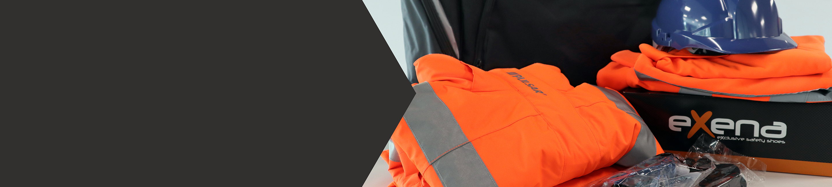 A black bag is behind orange hivis jackets, a shoe box, hard hat, gloves and goggles in plastic wrappers.