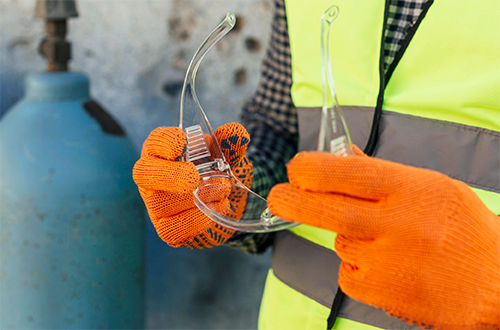 Two hands in orange gloves holding safety goggles in front of his chest