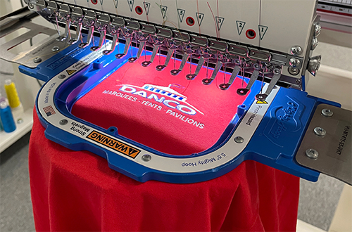 Close up of a Danco logo on a red shirt being embroidered on a Tajima Machine