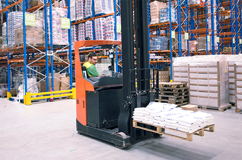 Man driving forklift with a pallet in a well-stocked warehouse